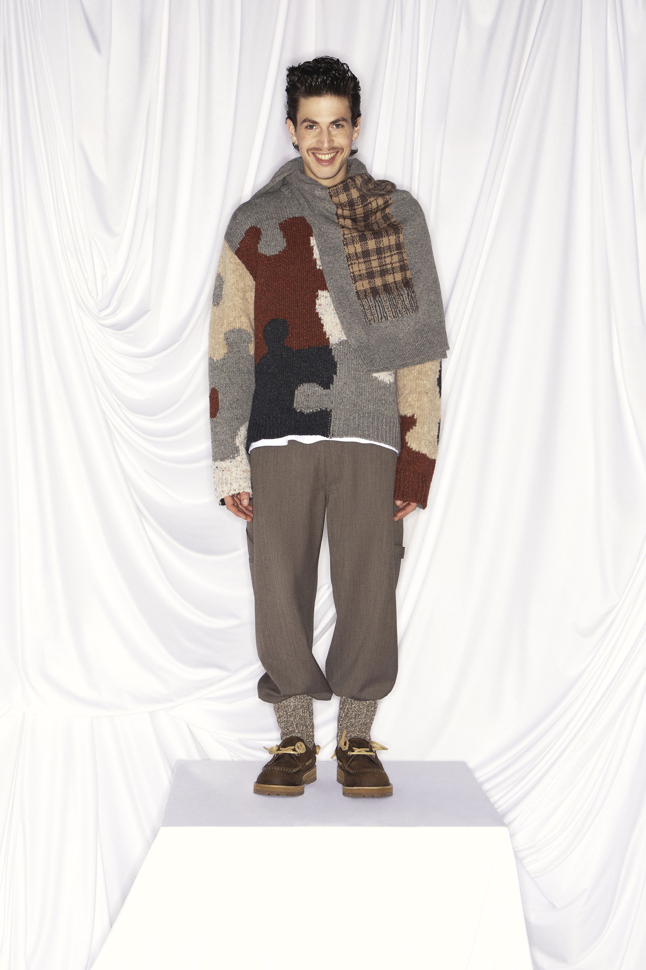 Moschino 26FW 以高度视觉化的“幽默符号”重申品牌精神，将玩具熊、笑脸图案、引号符号与拼贴针织转化为一种带有讽刺意味的时装语言。柔软针织与日常廓形承载强烈图像，使童真与荒诞并置，既像一场时尚游乐园，也是一种对当代消费文化的调侃。系列刻意拒绝克制美学，用直观情绪与符号刺激重新激活 Moschino 的反叛基因-顽石频道趋势研究